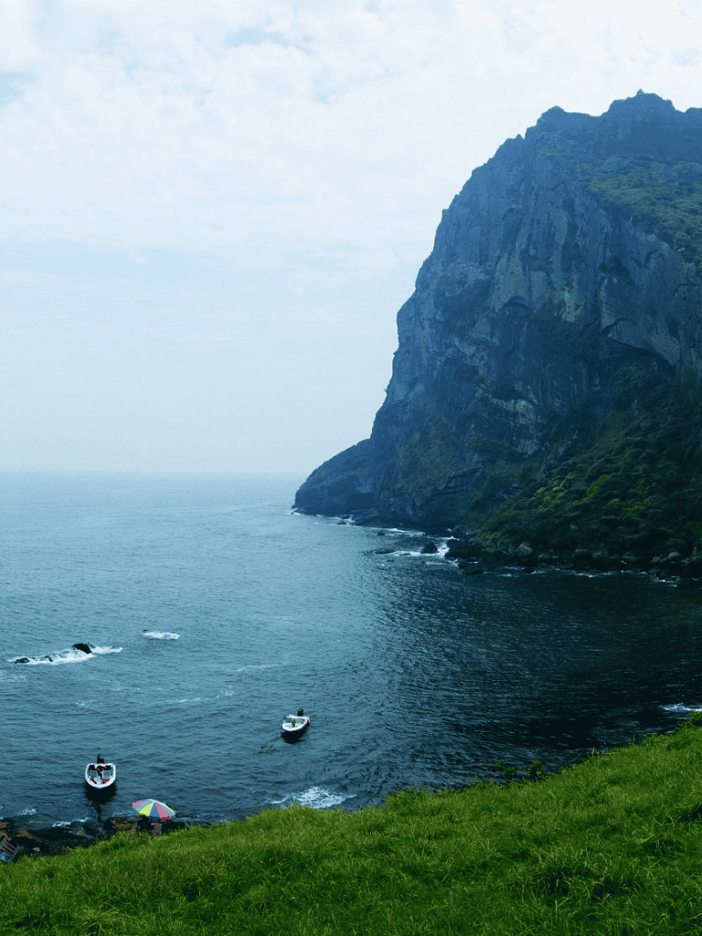 Majestic coastal cliffs with boats and lush green landscape, scenic ocean view for travel and adventure content.