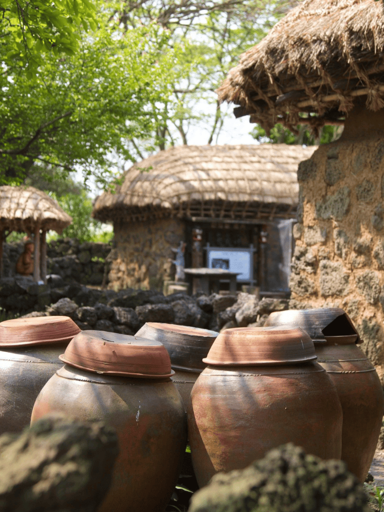 Traditional clay pots in a rural setting with stone huts and thatched roofs, showcasing cultural heritage.