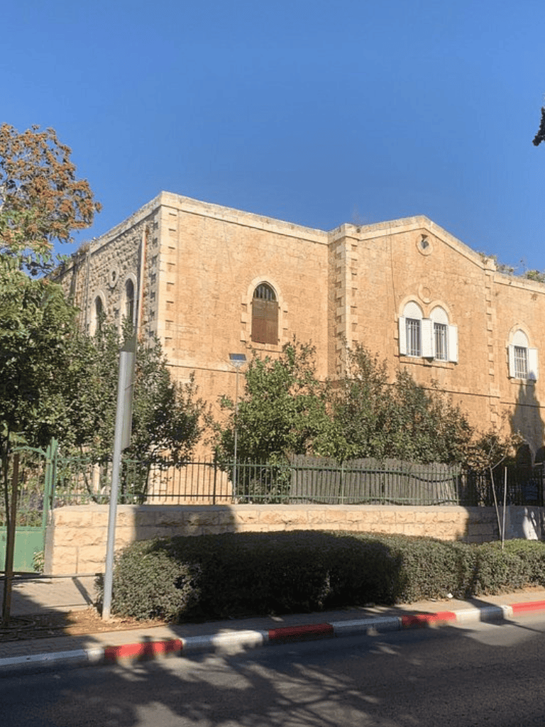 Ancient stone building with arched windows and lush greenery, under a clear blue sky.