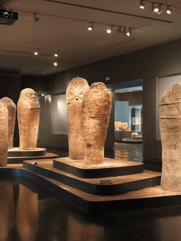 Ancient Egyptian sarcophagi display in a museum exhibit with modern lighting.