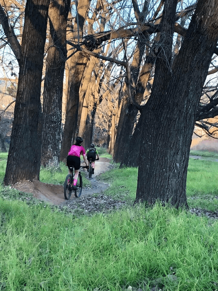 Girls riding mountain bikes through a wooded trail in spring nature.