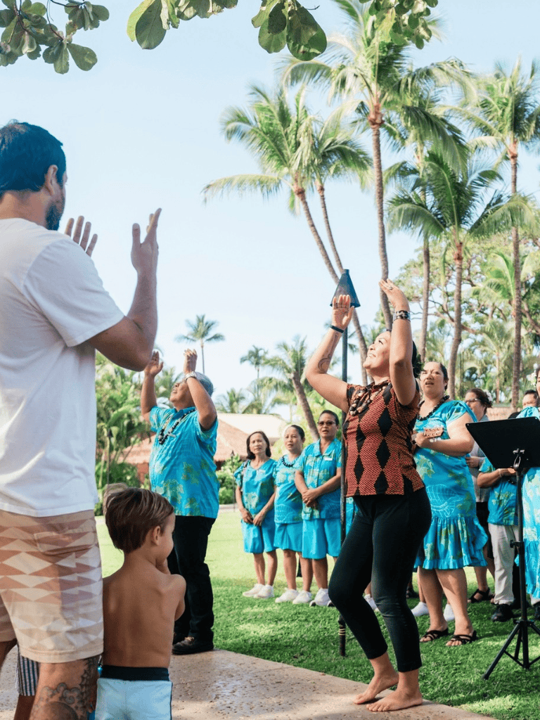 A woman dancing outdoors with group of people enjoying a cultural event under palm trees.