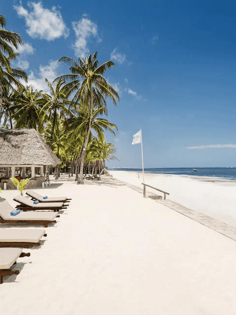 Palm trees on a tropical beach with lounge chairs and thatched huts, perfect for vacation planning.