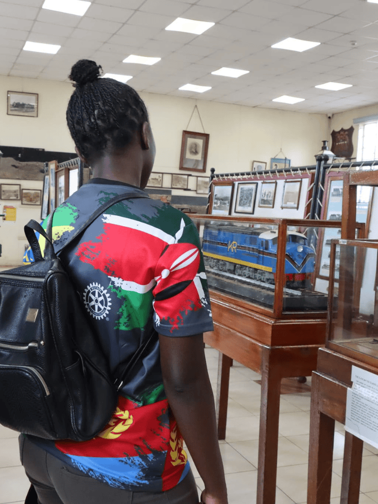 Colorful Kenyatta-themed shirt showcasing Kenya's heritage and rotary symbol at a museum exhibit of model trains and historical photos.
