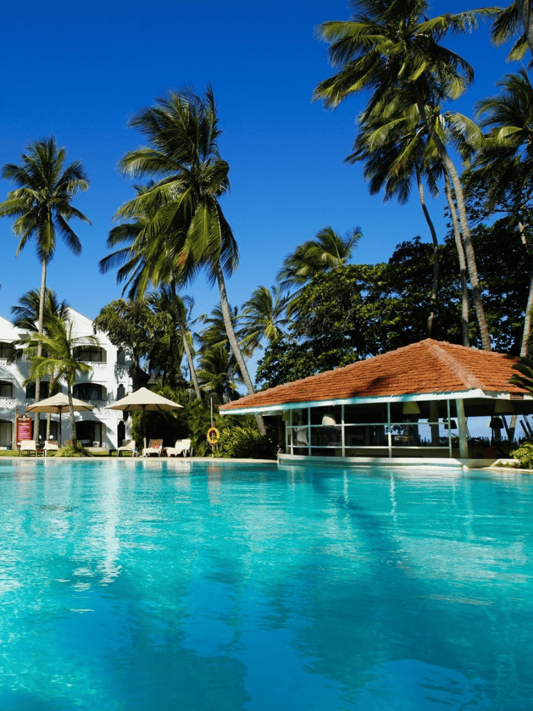 Tropical resort pool with palm trees and cabana under blue sky.