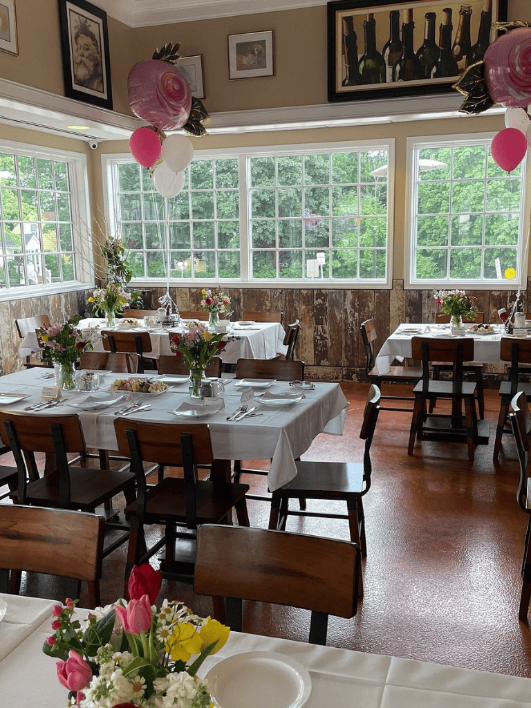 Colorful birthday celebration setup with balloons and floral arrangements in a cozy, well-lit restaurant with large windows.