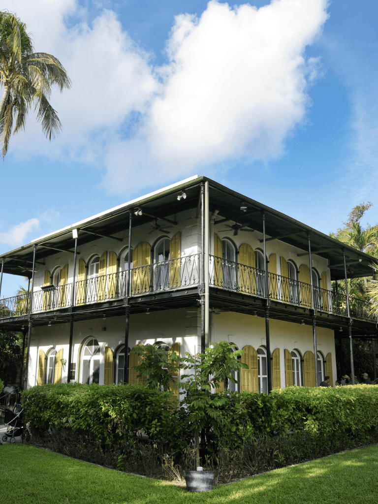 Historic two-story building with arched windows and yellow shutters, surrounded by lush greenery.