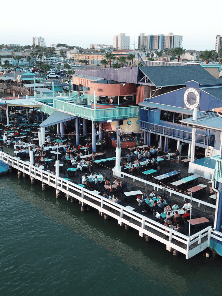 Vibrant seaside restaurant with outdoor patio, overlooking water, with bustling dining scene.