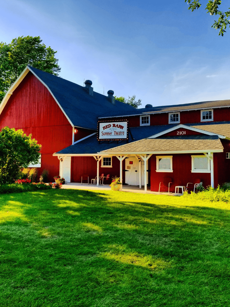 Rustic Red Barn Theater with lush green lawn and clear blue sky, perfect for summer entertainment and family outings.