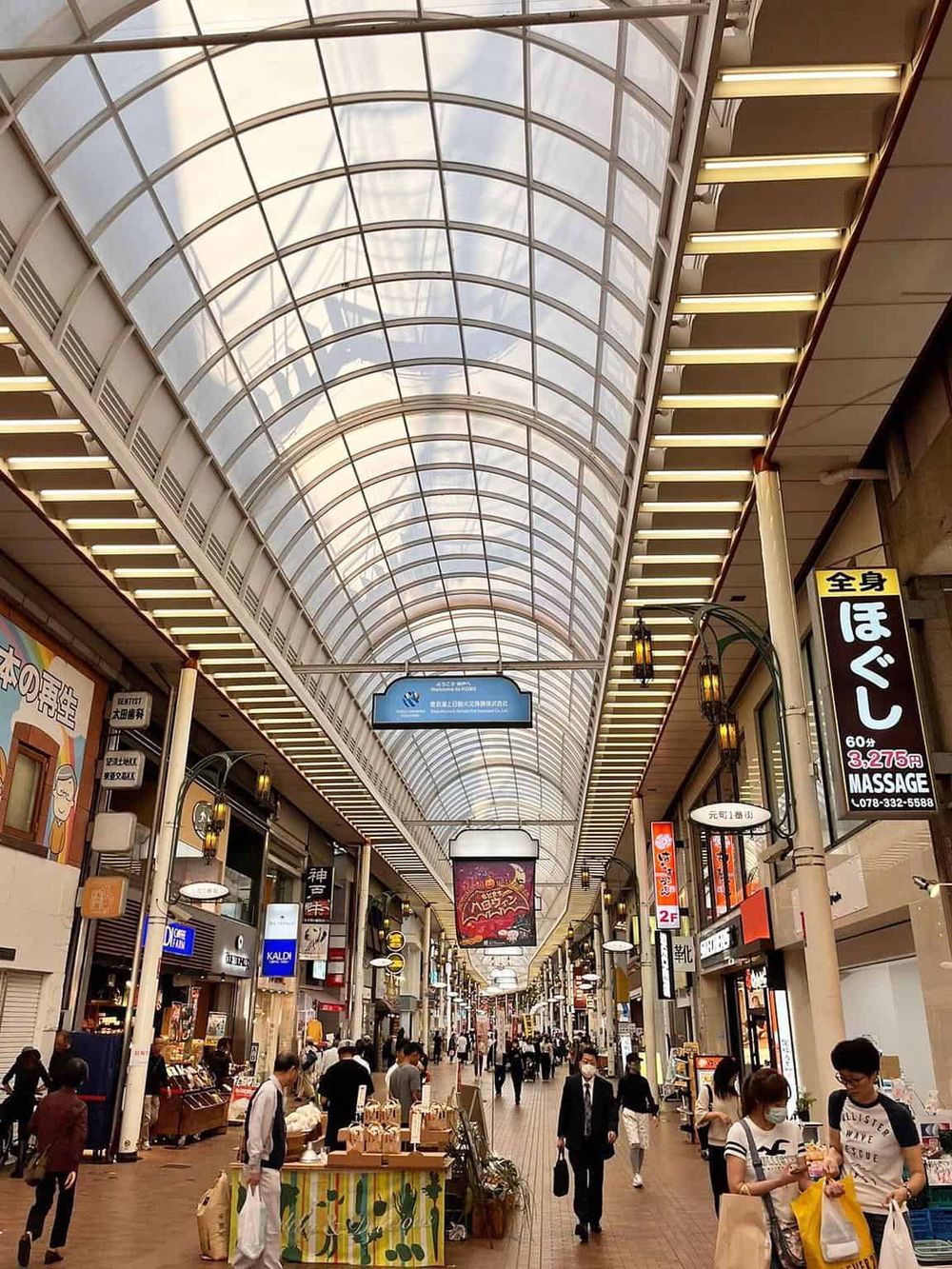 Bright indoor shopping arcade with glass vaulted ceiling, retail stores, and shoppers in Japan.