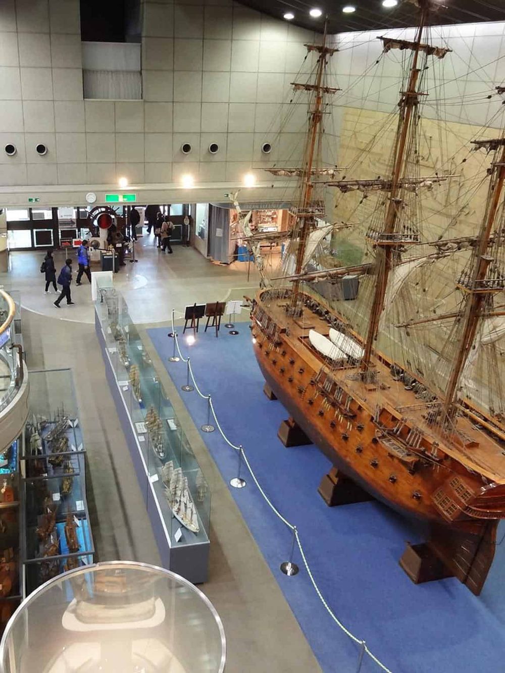 Vintage sailing ship model exhibit in maritime museum, indoor display with visitors in background.