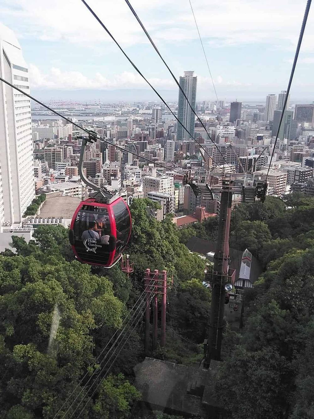 Red gondola cable car over city skyline during daytime, scenic urban transportation attraction.