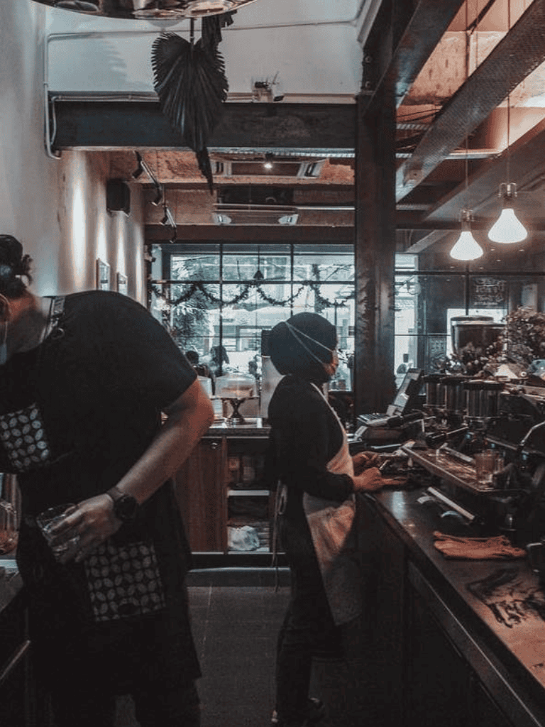 Busy coffee shop with barista preparing drinks and customer ordering at the counter, modern decor, cozy ambiance, winter decorations.