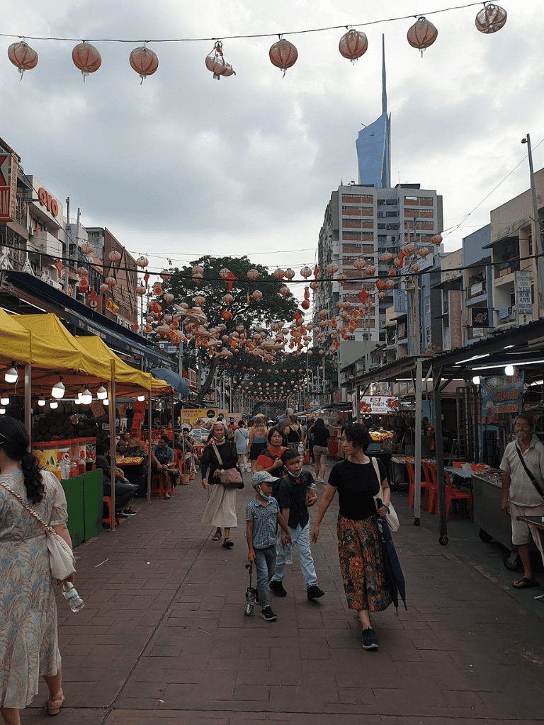 Colorful street market in Chinatown with lantern decorations and diverse shoppers, showcasing urban culture and vibrant commerce.