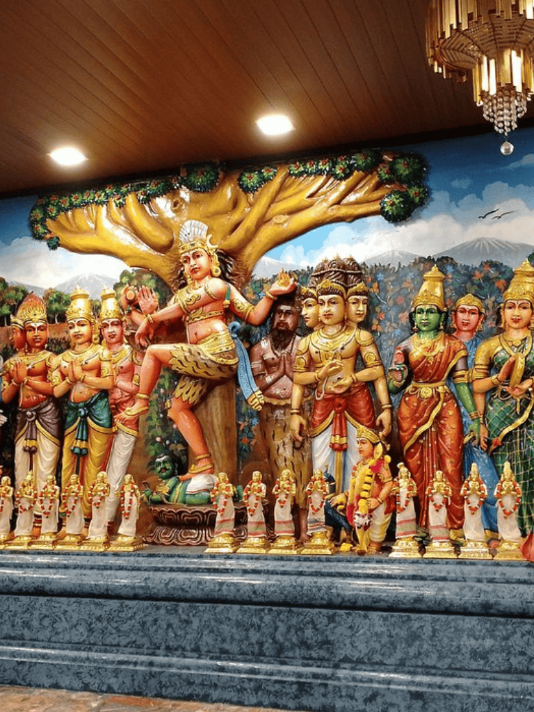 Colorful Hindu temple sculptures depicting various deities and mythological figures under a large tree.