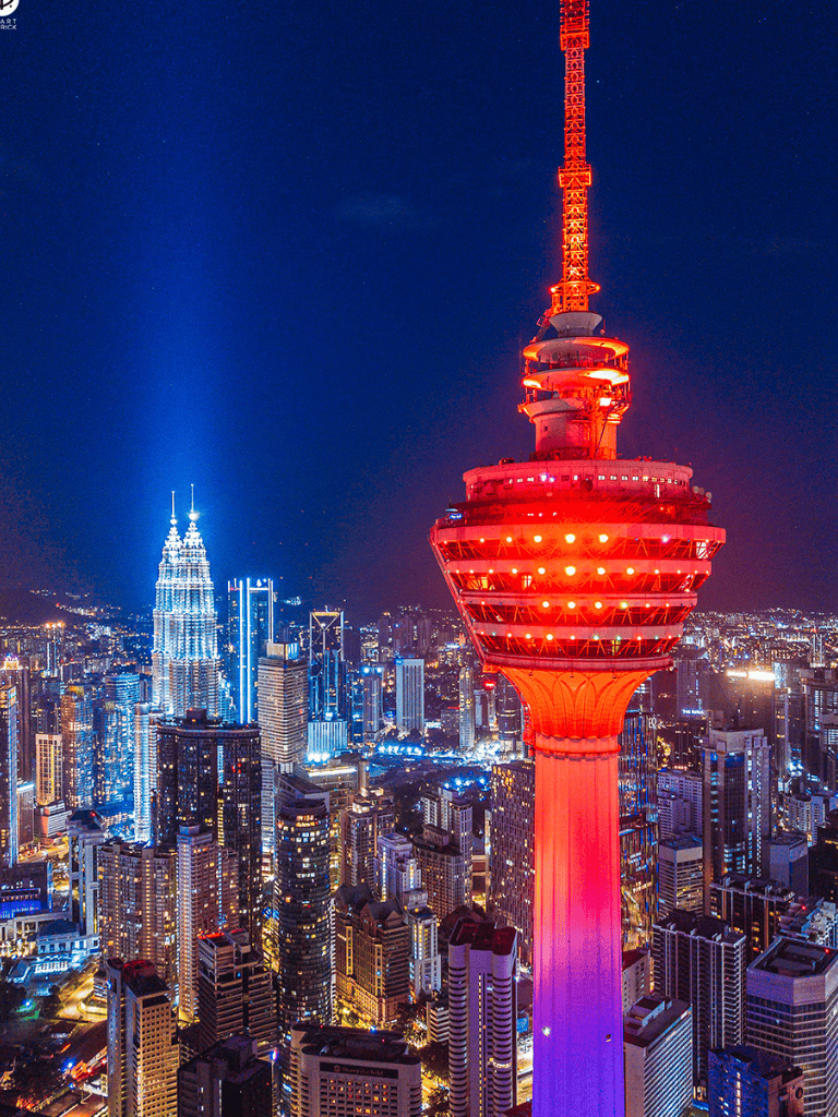 Iconic Kuala Lumpur Tower illuminated at night with city skyline in the background.