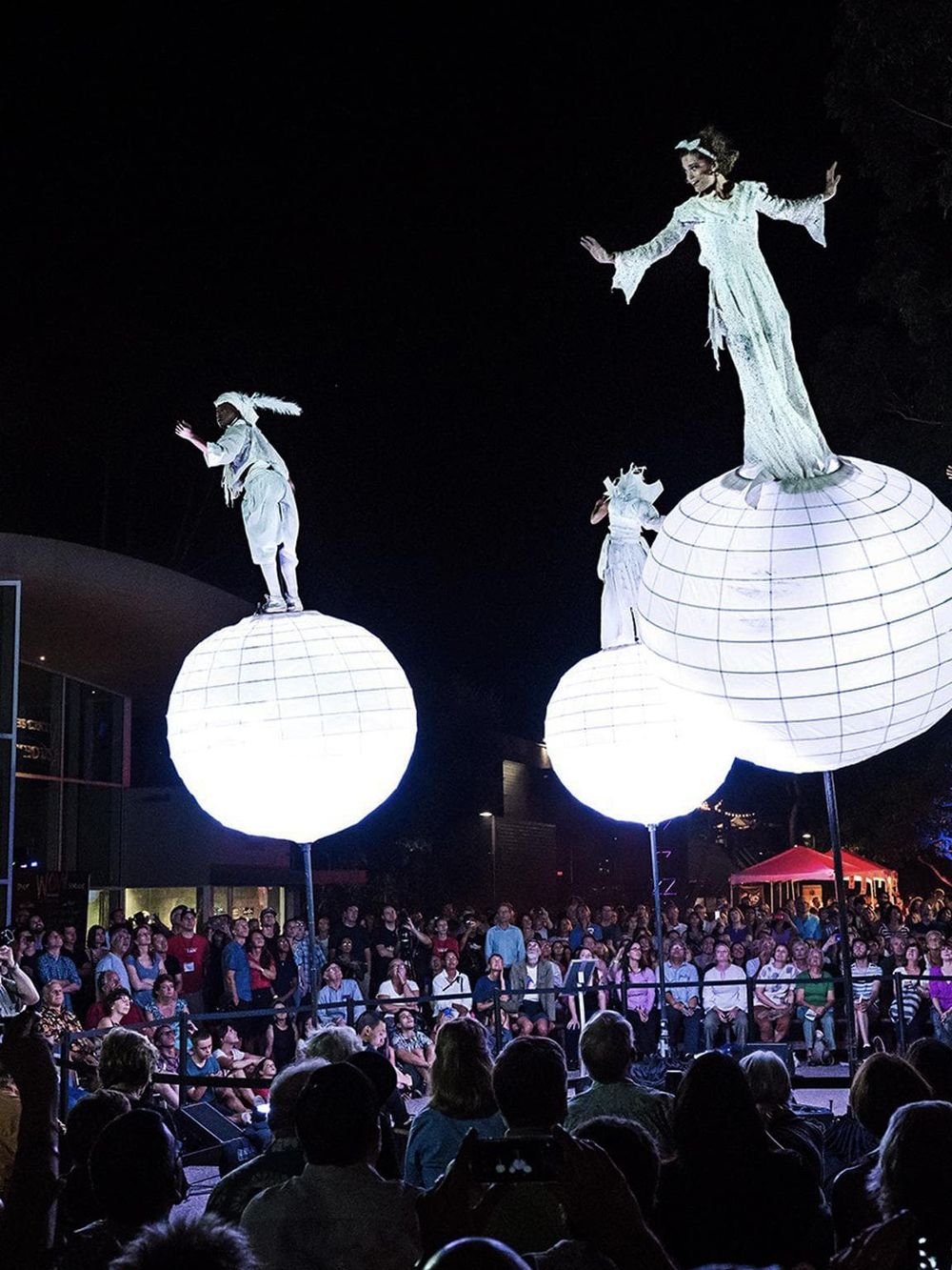 Imaginative night performance with illuminated floating performers on globes, captivating large audience.