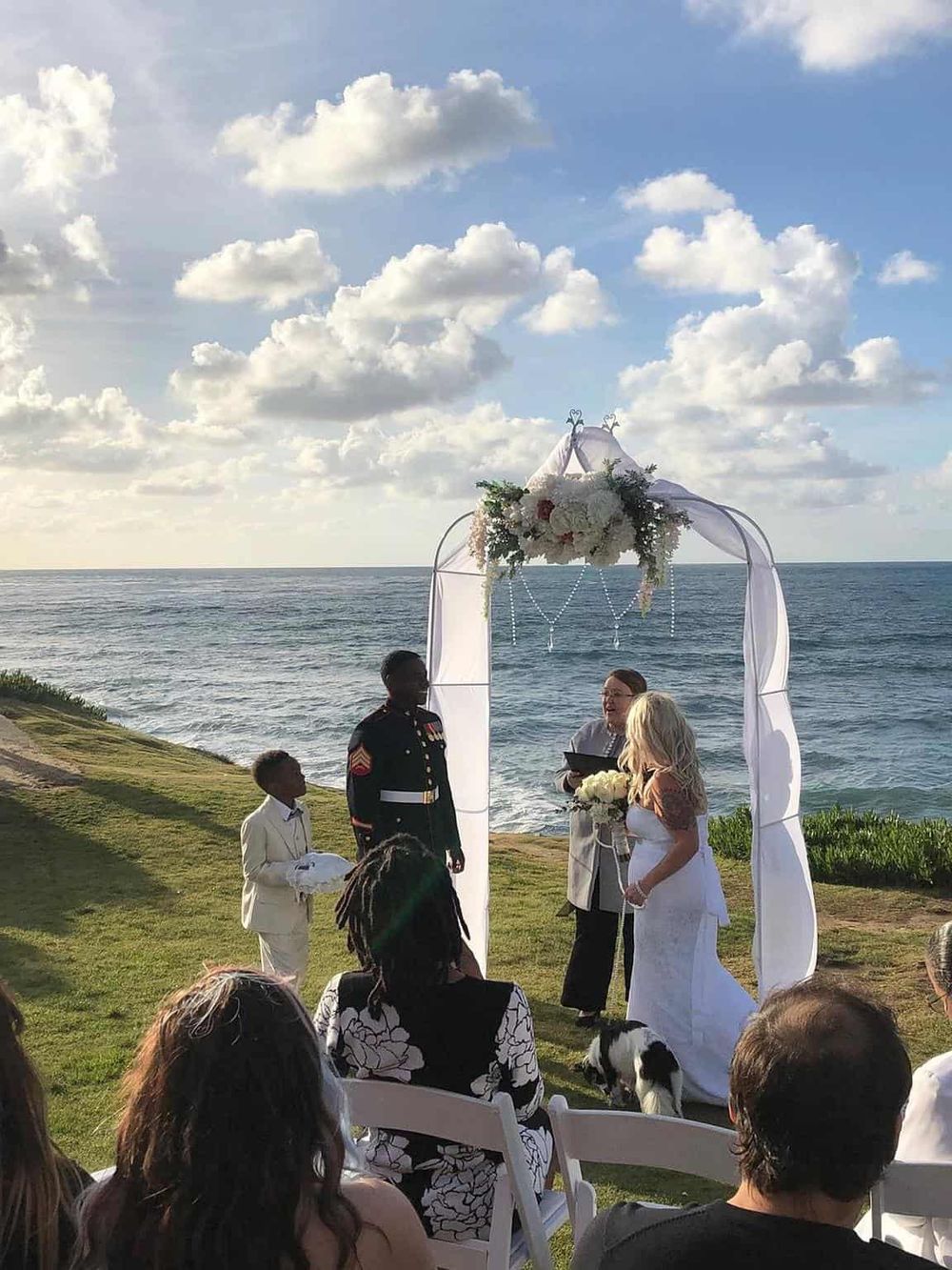Elegant beachfront wedding ceremony at sunset with ocean backdrop, floral arch, and outdoor seating.