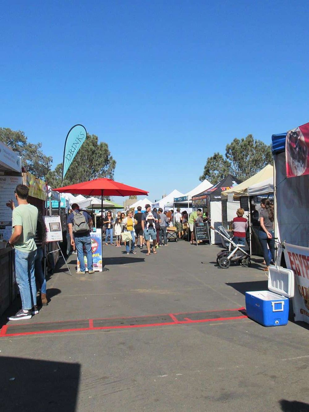 Outdoor food festival with vendor tents and crowd, sunny sky, lively event atmosphere.