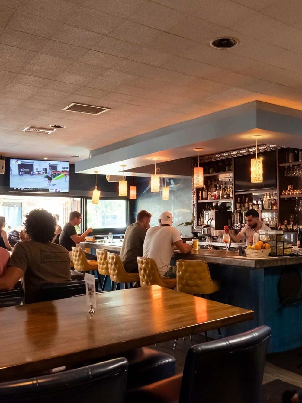 Cozy bar interior with customers enjoying drinks and socializing, modern decor, and hanging pendant lights.