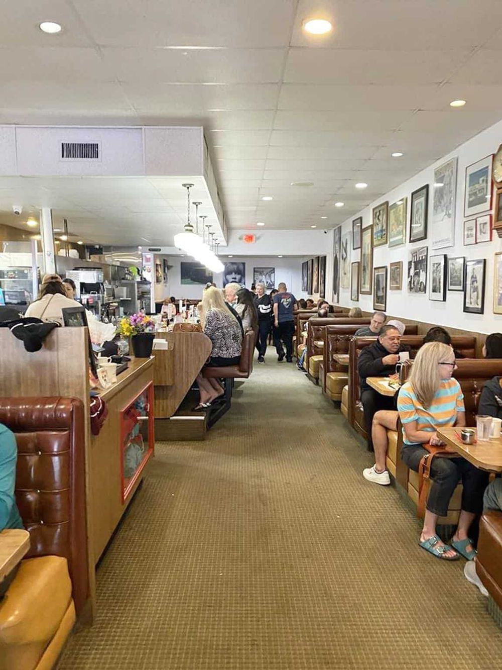 Cozy diner interior with booth seating and artwork wall decor, busy with diverse customers enjoying meals.