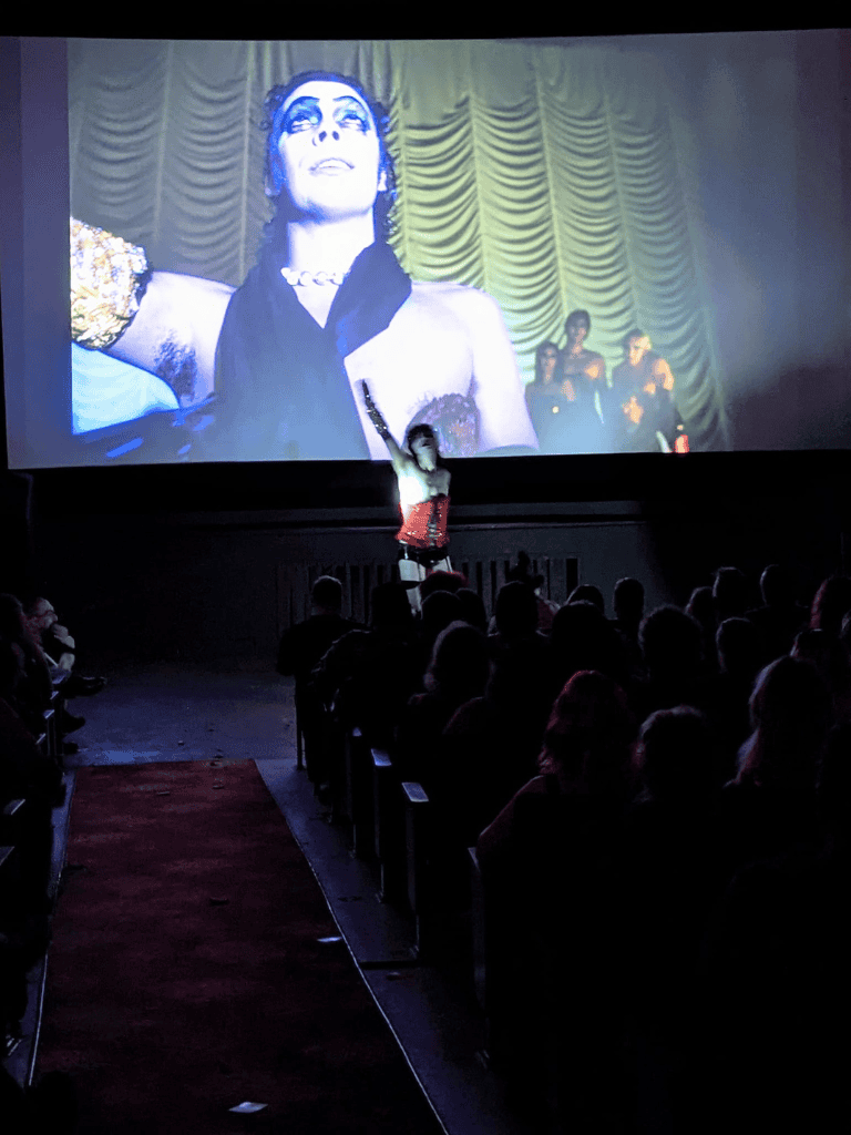 Blurred image of a performer on stage at QuestForDirections event, audience watching live theater show.
