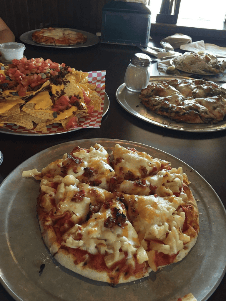 Cheese pizza with toppings and Mexican nachos on a restaurant table.