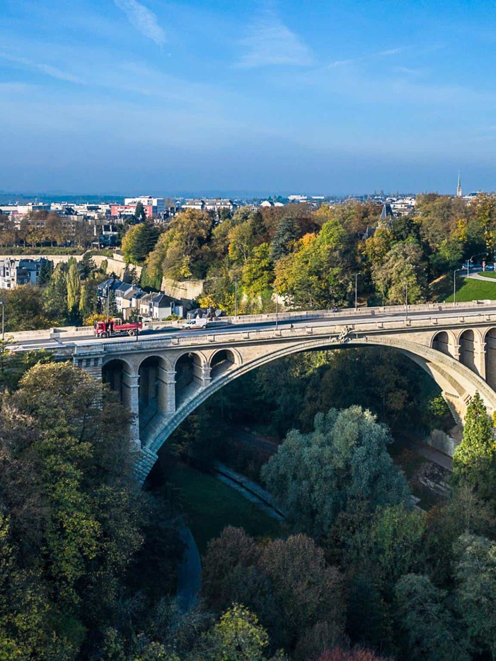 Scenic view of a bridge over a green valley with a cityscape in the background on a clear day.