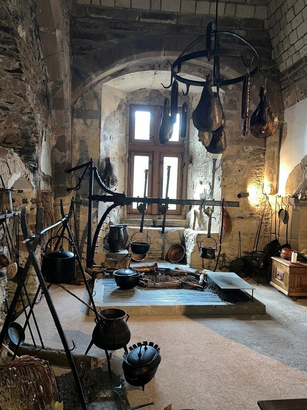 Rustic medieval kitchen with hanging cured meats, cast iron pots, and stone walls, showcasing traditional European culinary heritage.