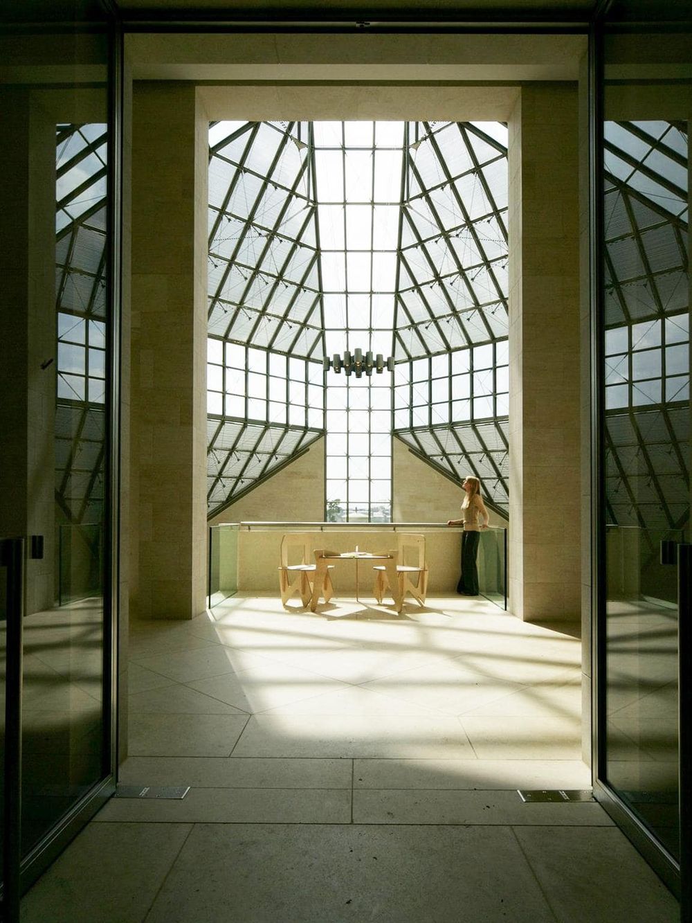 Bright glass atrium with modern architecture, ample natural light, and a woman enjoying the space.