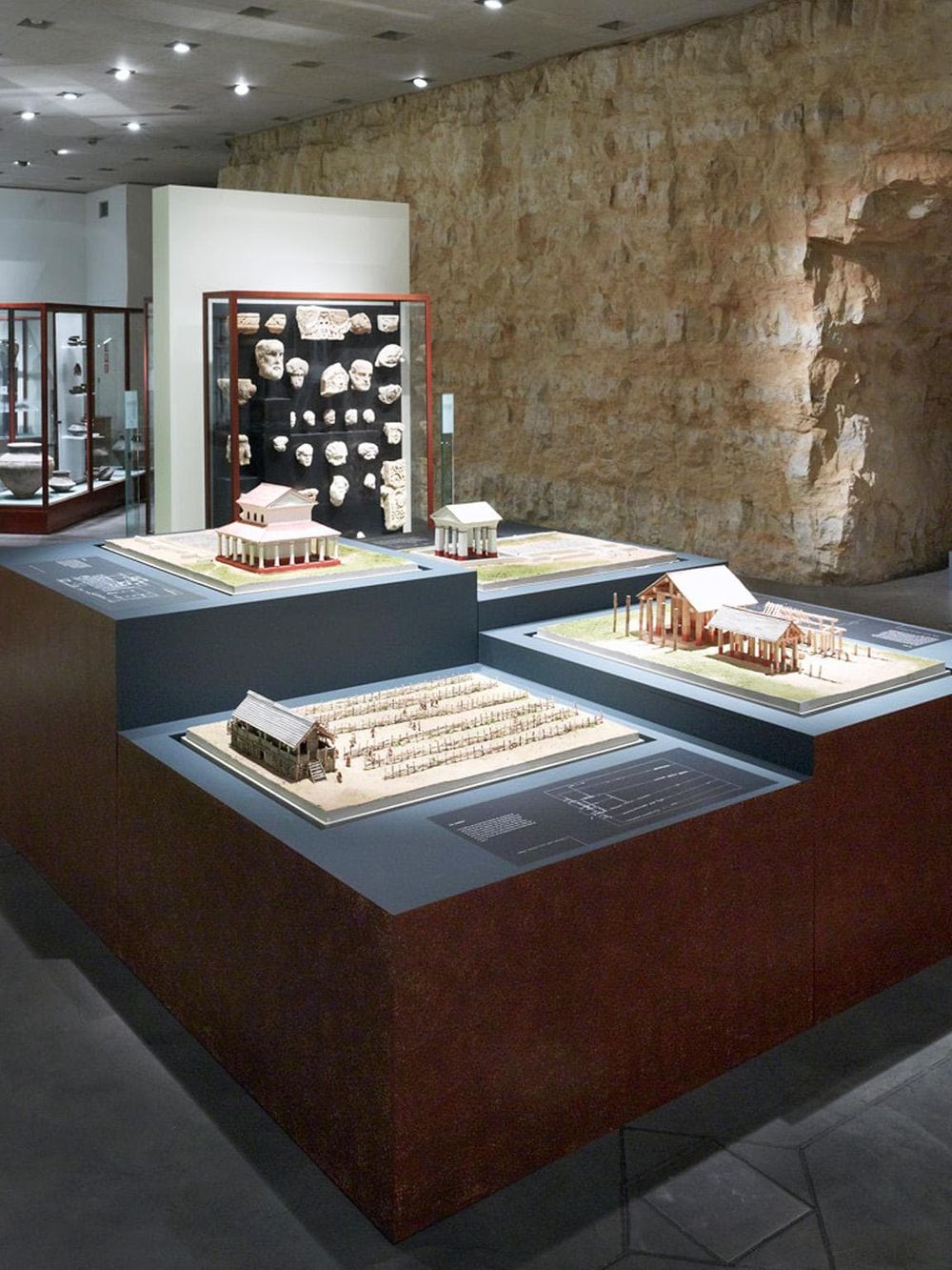 Ancient Greek architectural models and artifacts displayed in a museum exhibit for educational tours.