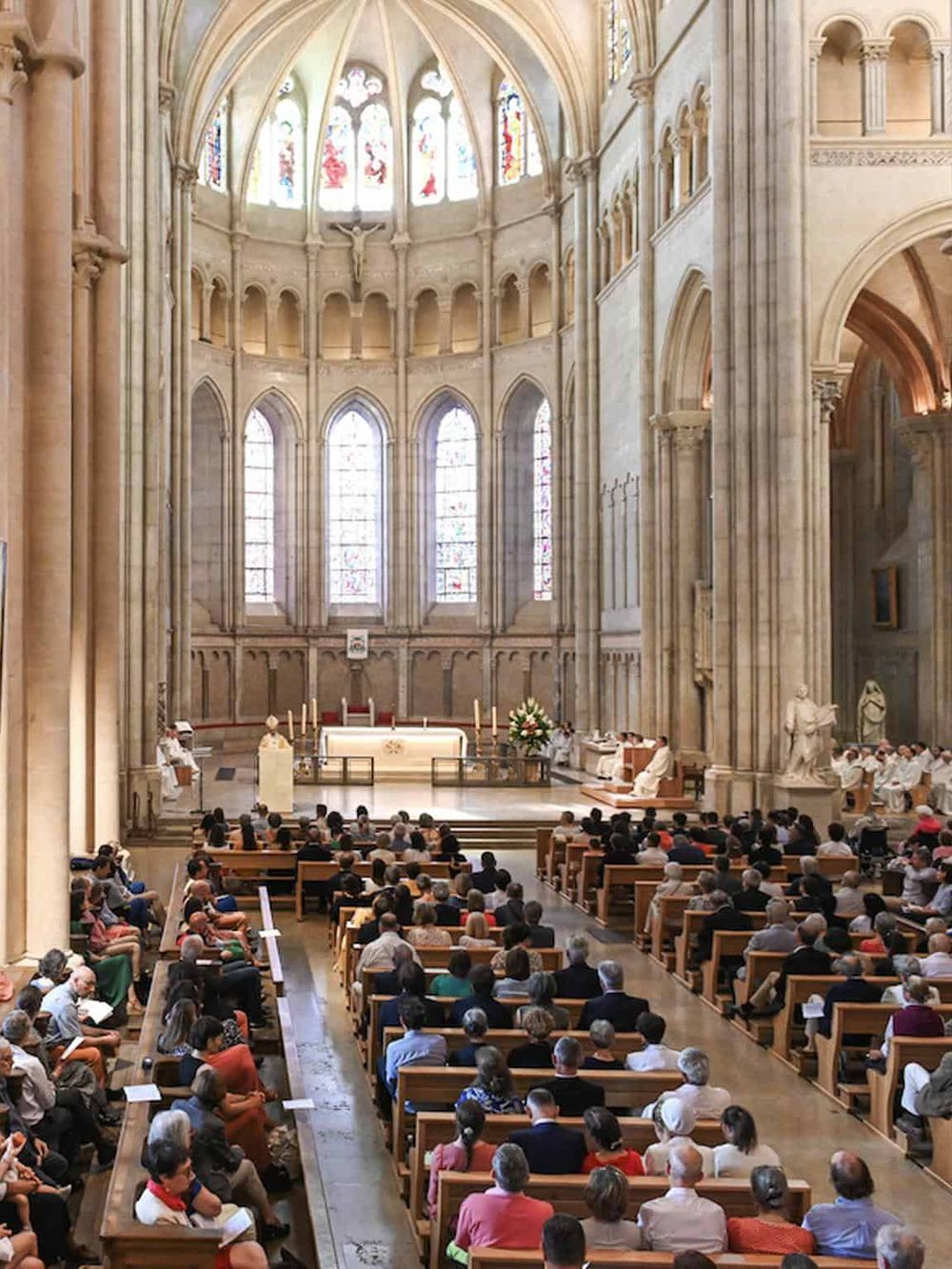 Stained glass windows in a grand cathedral with a congregation attending a service.