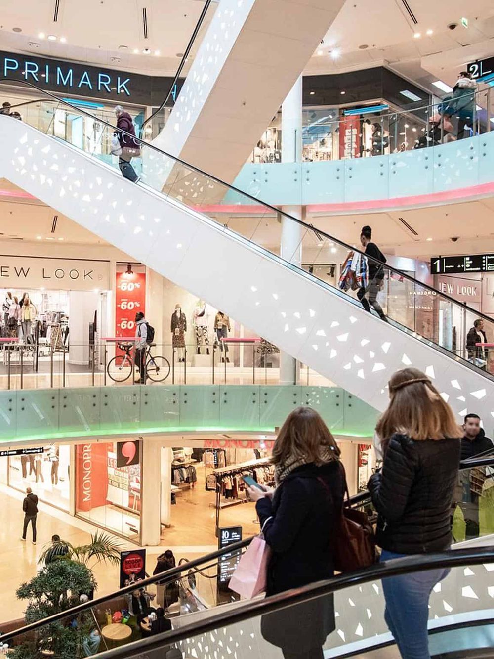 Bright shopping mall interior with escalators, retail stores, and shoppers at QuestForDirections.