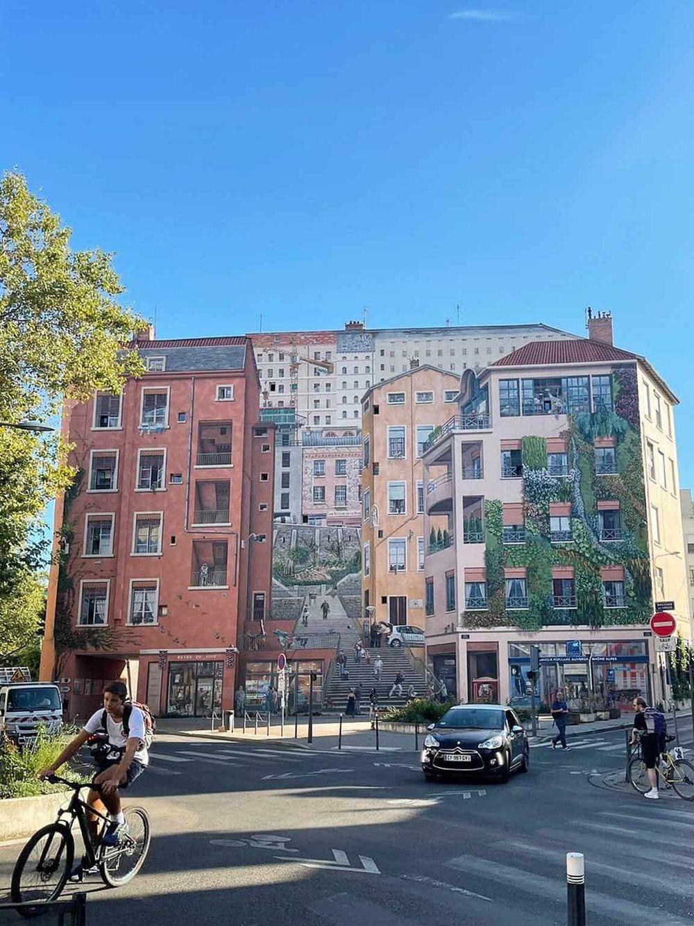 Colorful cityscape mural with stairs, buildings, and people cycling and walking in the sunny urban scene.