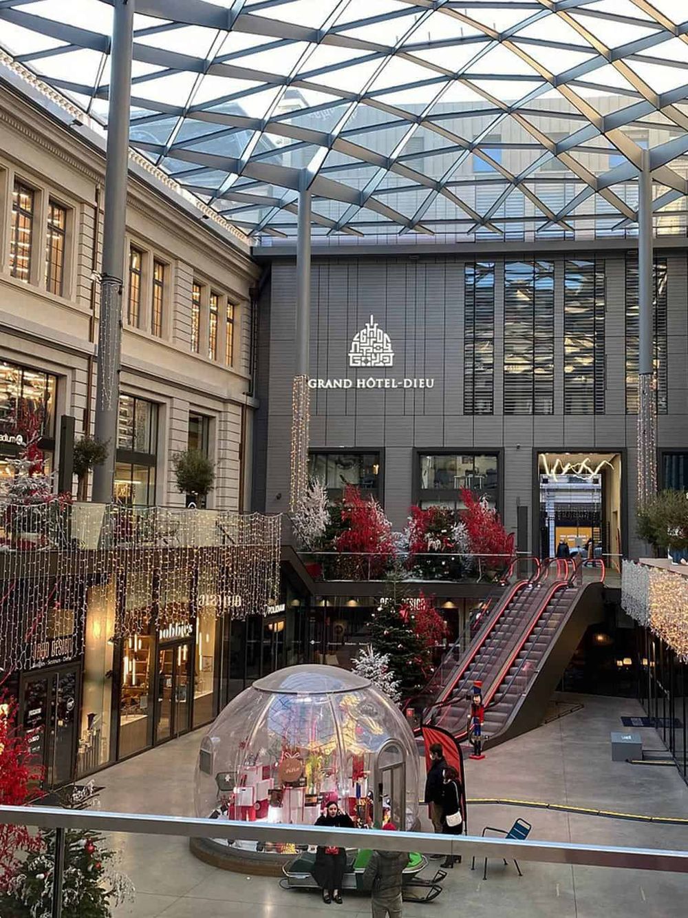 Vibrant indoor shopping mall decorated for Christmas, featuring a Christmas tree and festive lights, with Grand Hotel Dieu signage.