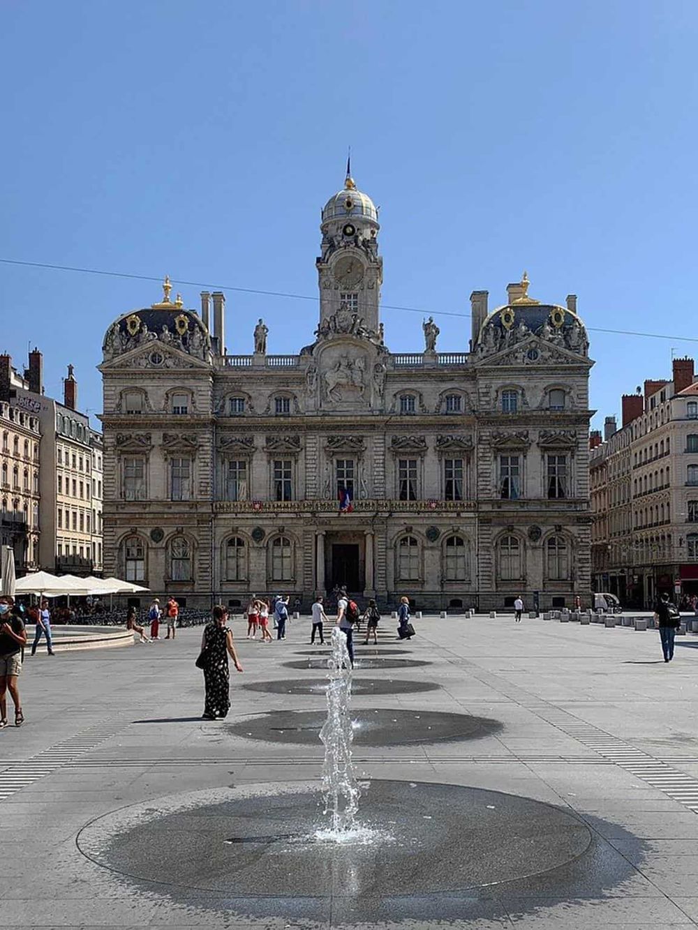 Historic city hall building in Marseille, France, with modern fountains and pedestrians in a vibrant city square.