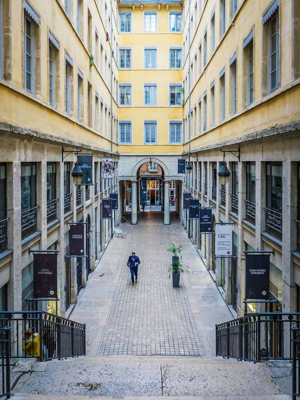 Bright yellow courtyard of an urban apartment complex with storefronts and person walking, modern city environment.