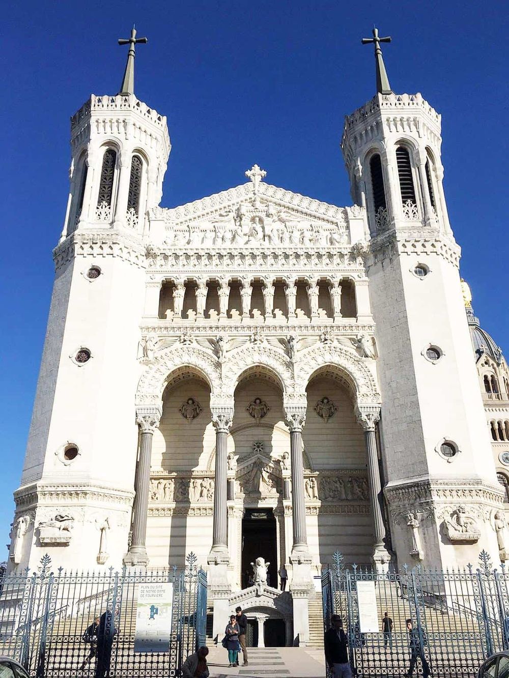 Majestic white cathedral with intricate architectural details and two towering spires against a bright blue sky.