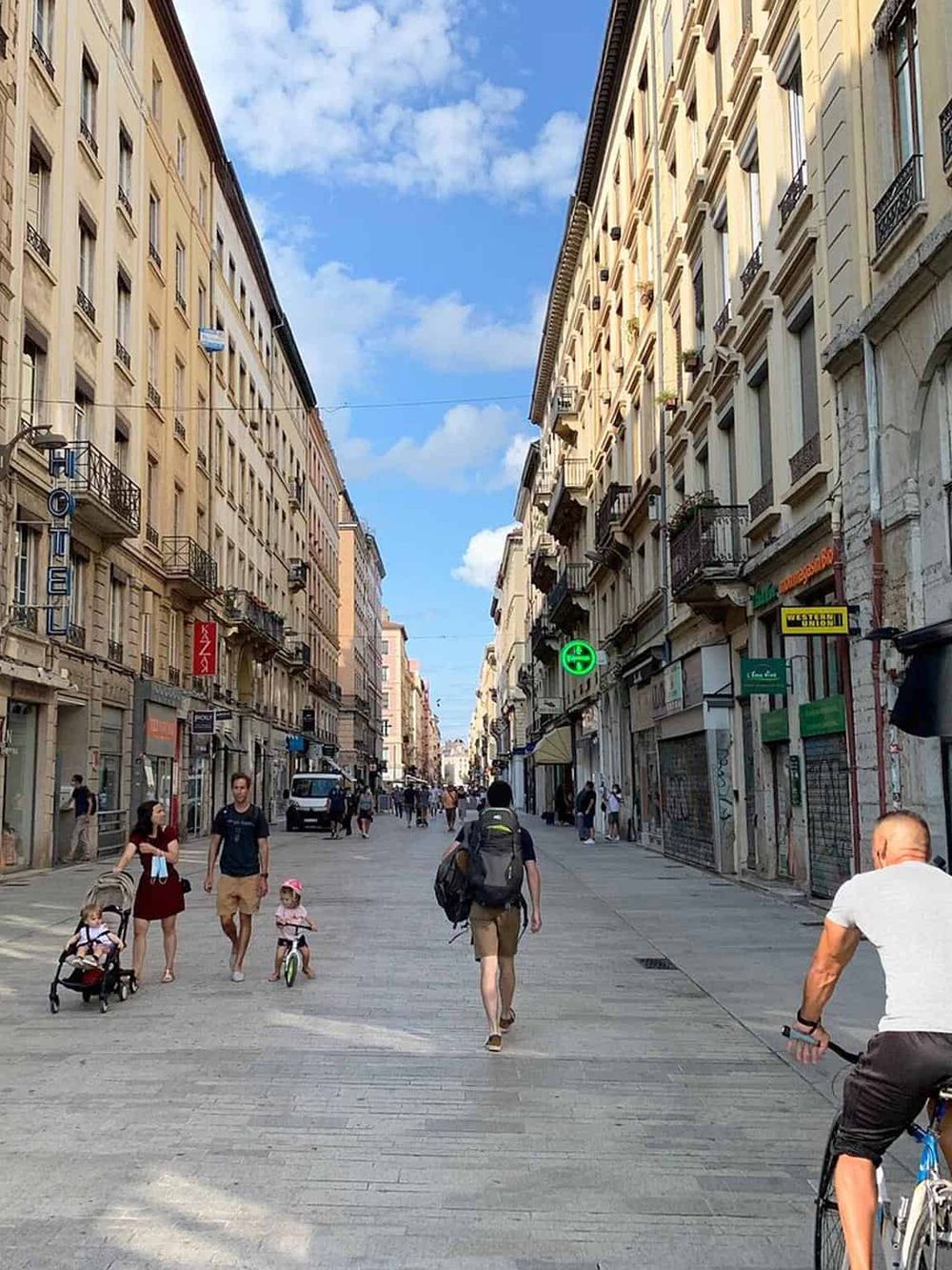 Bustling city street with pedestrians and cyclists, classic European architecture, and vibrant storefronts.