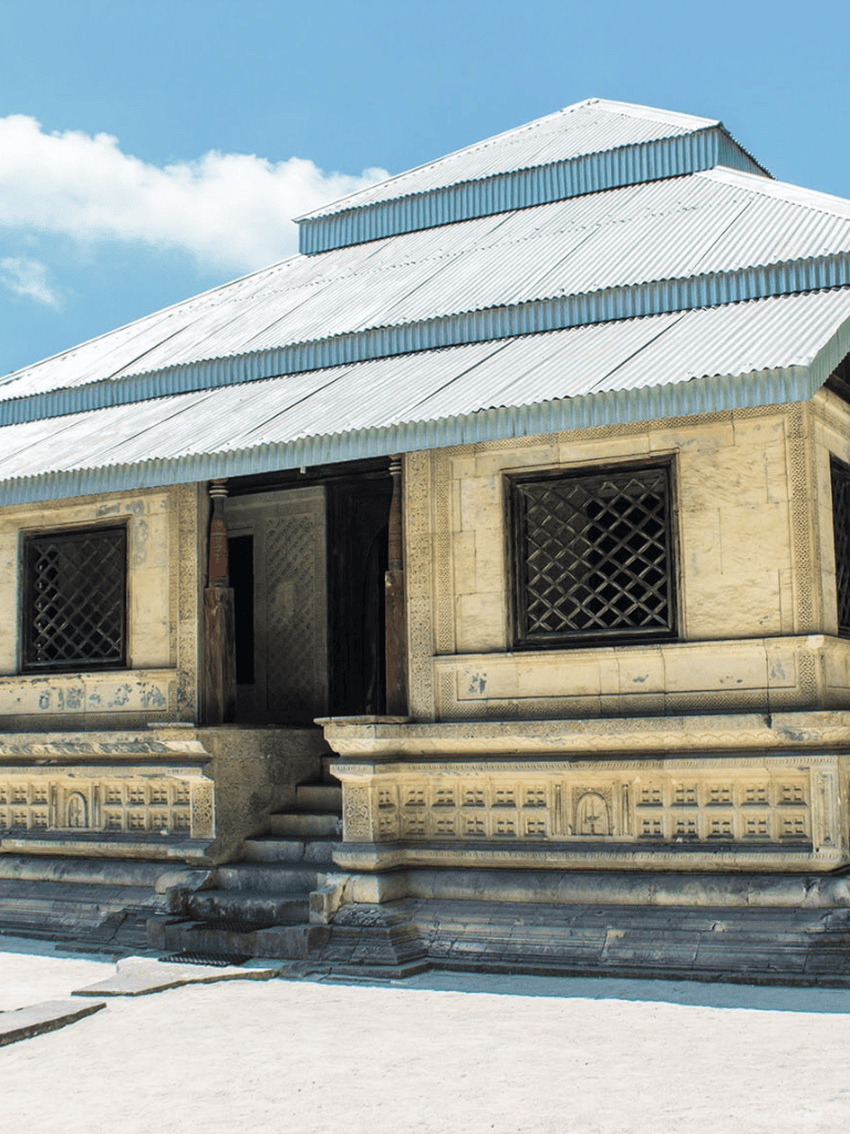 Ancient stone temple with intricate carvings and a metallic roof under a blue sky.