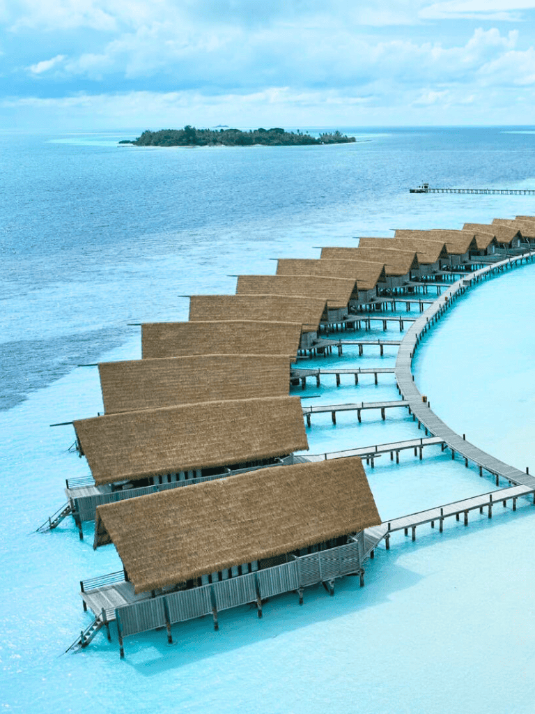 Overwater bungalows at a tropical resort with an ocean view and island in the background.