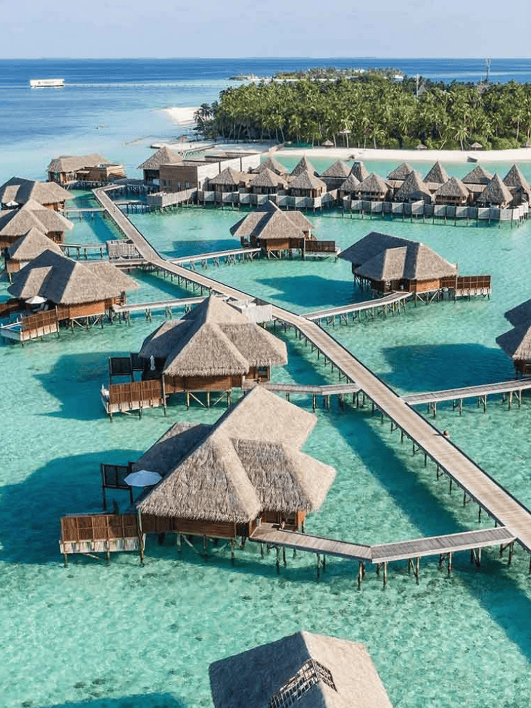 Overwater bungalows and pools at a tropical resort with crystal-clear water and lush greenery in the background.