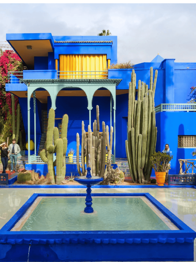 Vibrant blue Moroccan-style building with cactus garden, fountain, and decorative architecture.