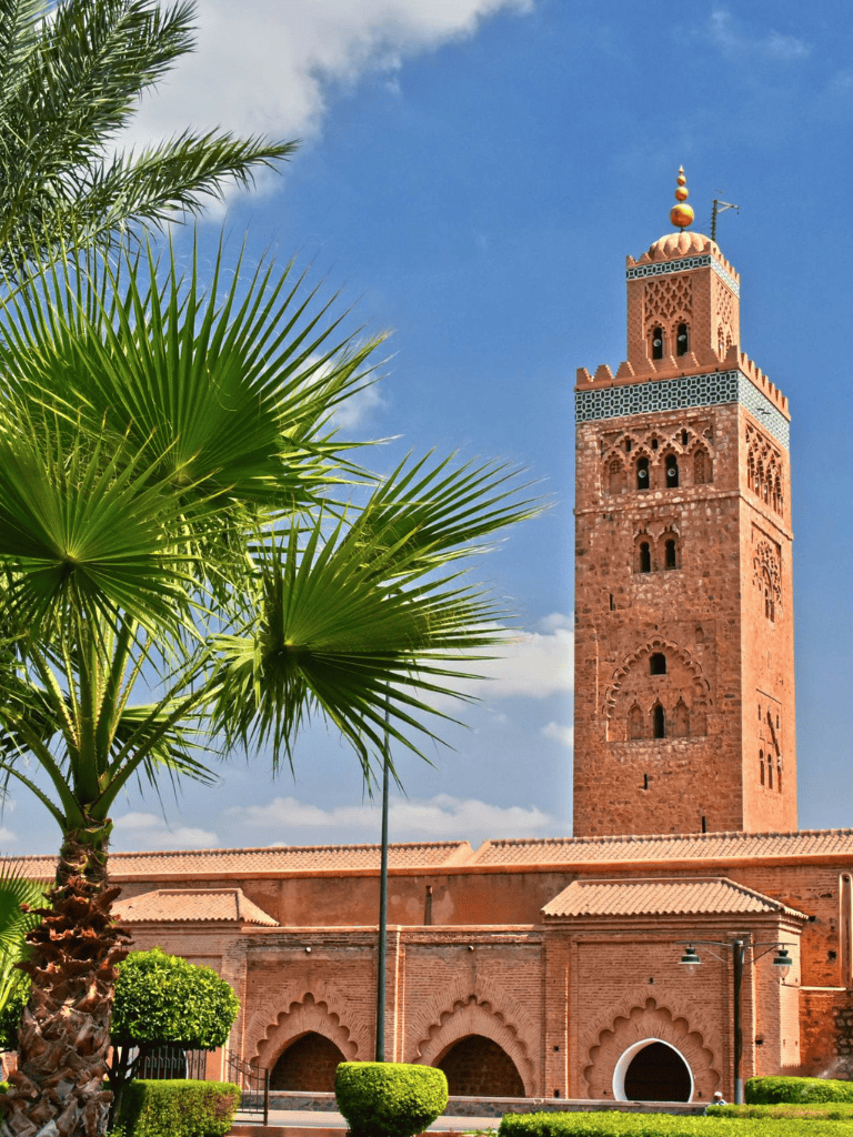 Ancient Moroccan minaret with lush palms, bright blue sky, and historic architecture.