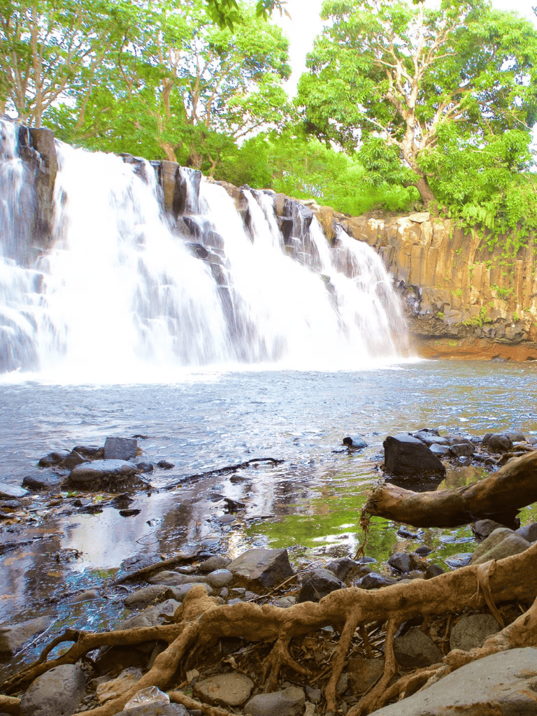 Waterfall with lush green trees and rocky riverbed, scenic natural outdoor landscape.