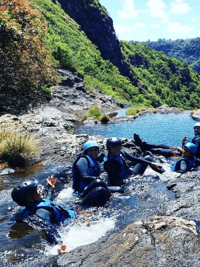 Adventure water rafting in lush green canyon with group of people wearing helmets and life jackets.