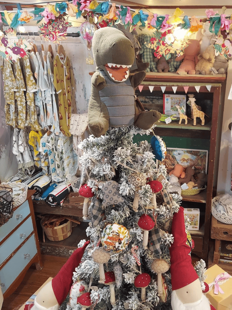 Cute stuffed dinosaur toy on a decorated Christmas tree in a cozy boutique store.