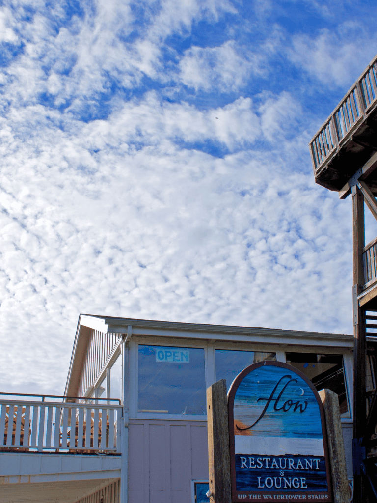Bright blue sky with clouds above a waterfront restaurant and lounge, showcasing scenic views and easy access via Watertower stairs.