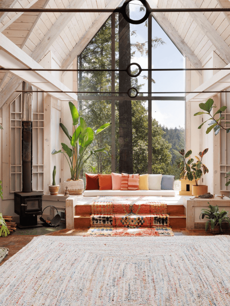 Bright living room with large windows and lush indoor plants, showcasing cozy decor and natural light.