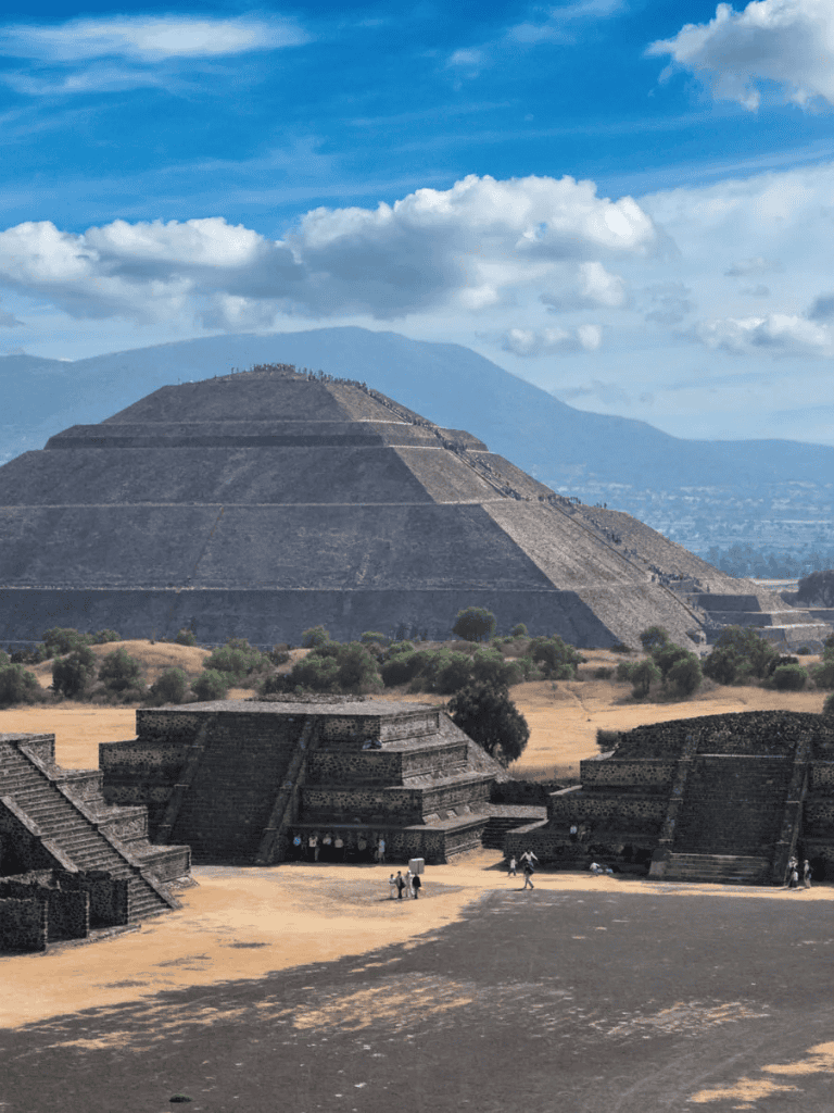 Ancient pyramid at Teotihuacan with blue sky and mountainous background, historical Mexican archaeological site.